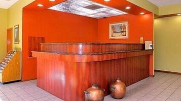 Un área de recepción con un mostrador curvo de madera, dos jarrones de cobre y un cuadro en la pared.