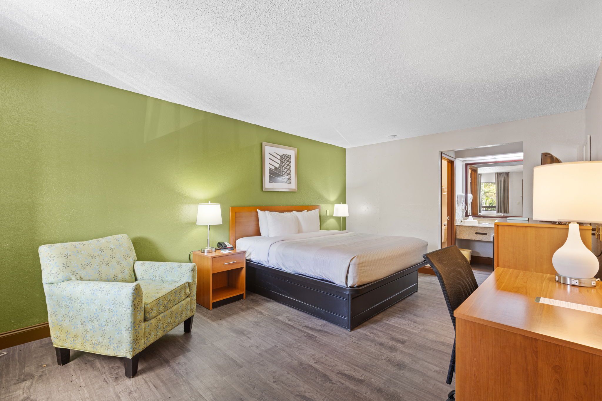 A hotel room with a bed, a chair, a desk, and a mirror.