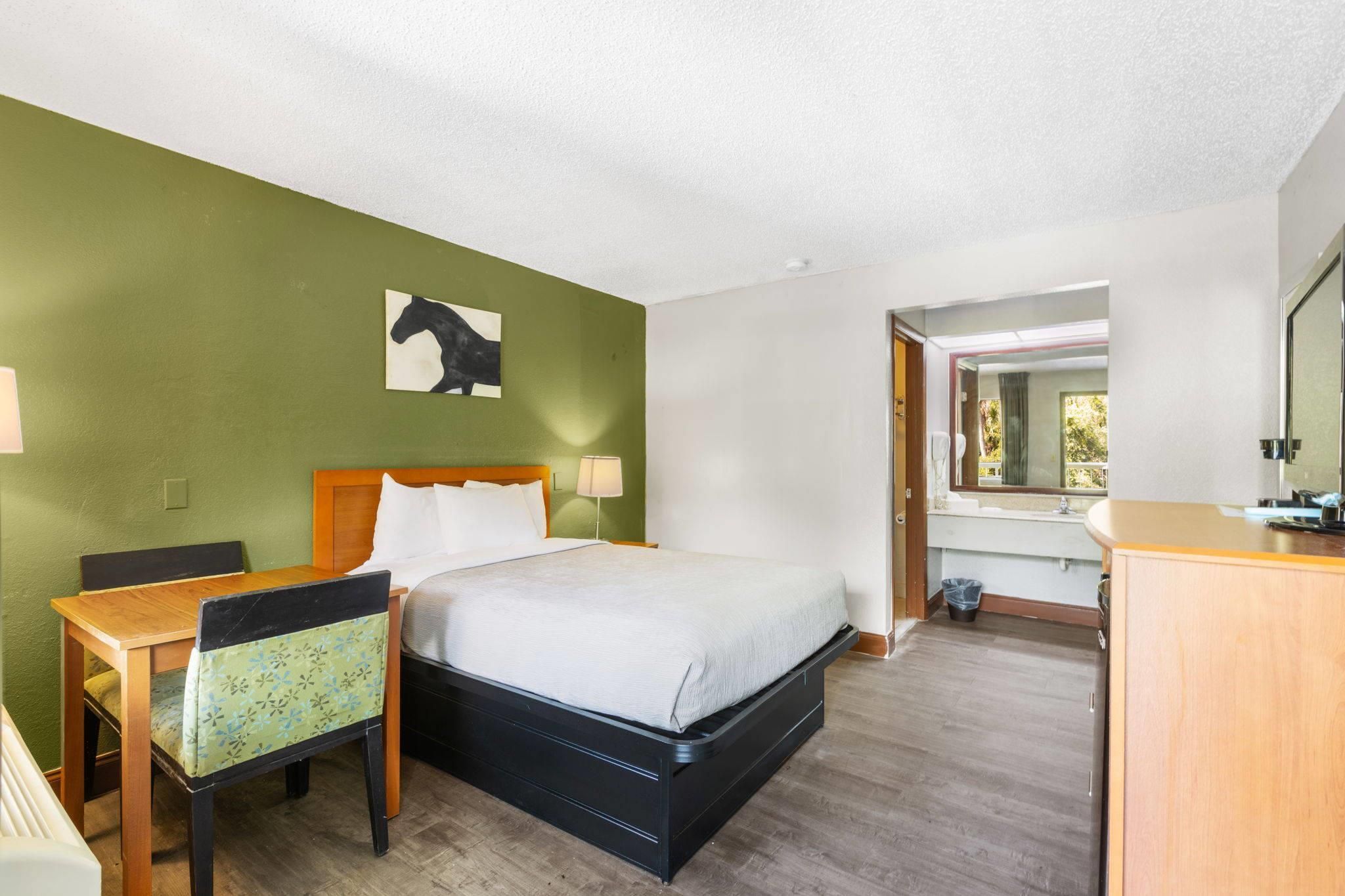 Habitación de hotel con cama, escritorio, silla, espejo y un cuadro de un caballo en la pared.