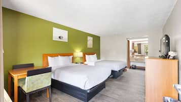 A hotel room with two beds, a desk, a chair, a small table, and a mirror.