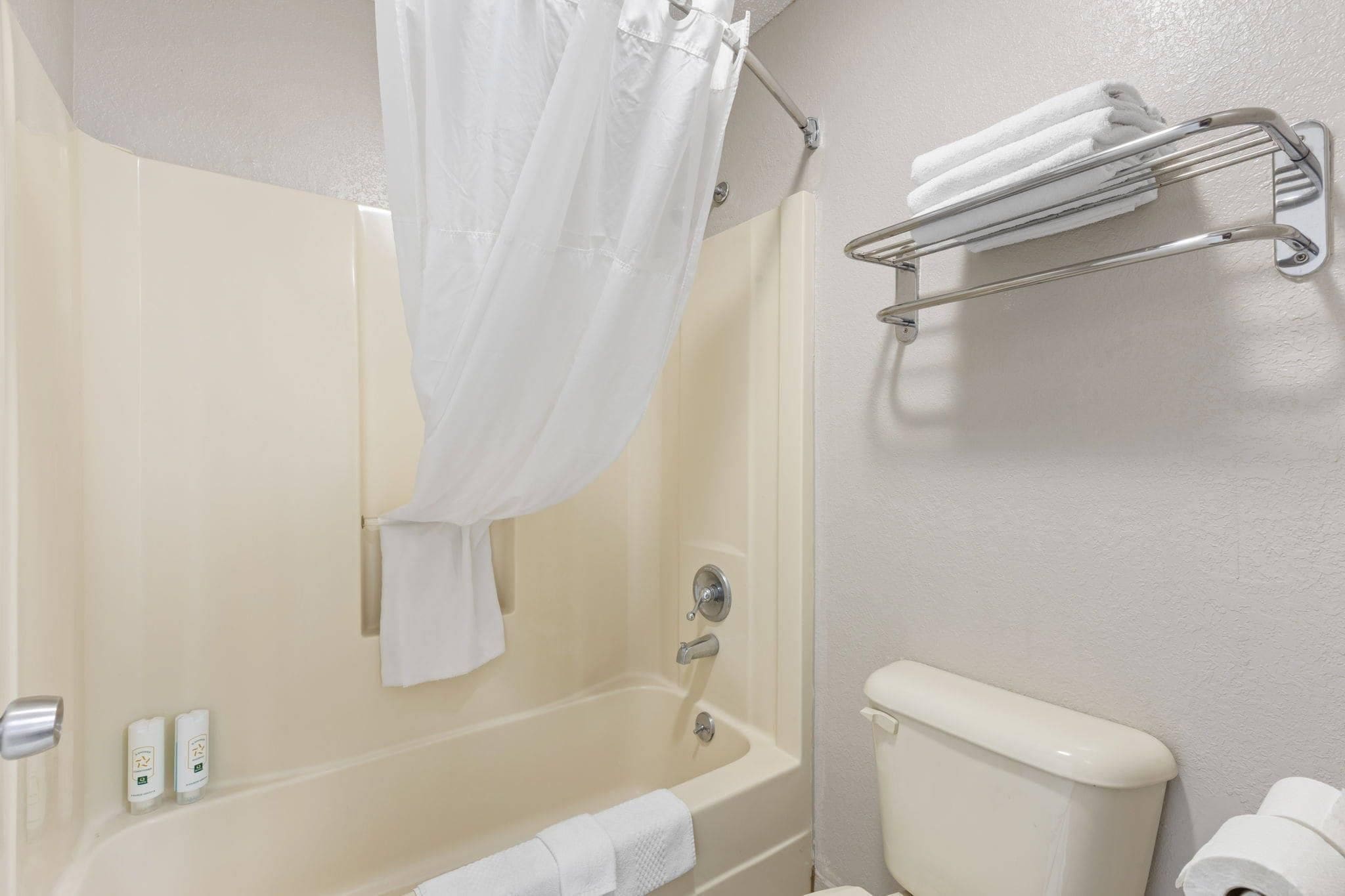 A bathroom with a bathtub, a shower curtain, a toilet, and a towel rack.