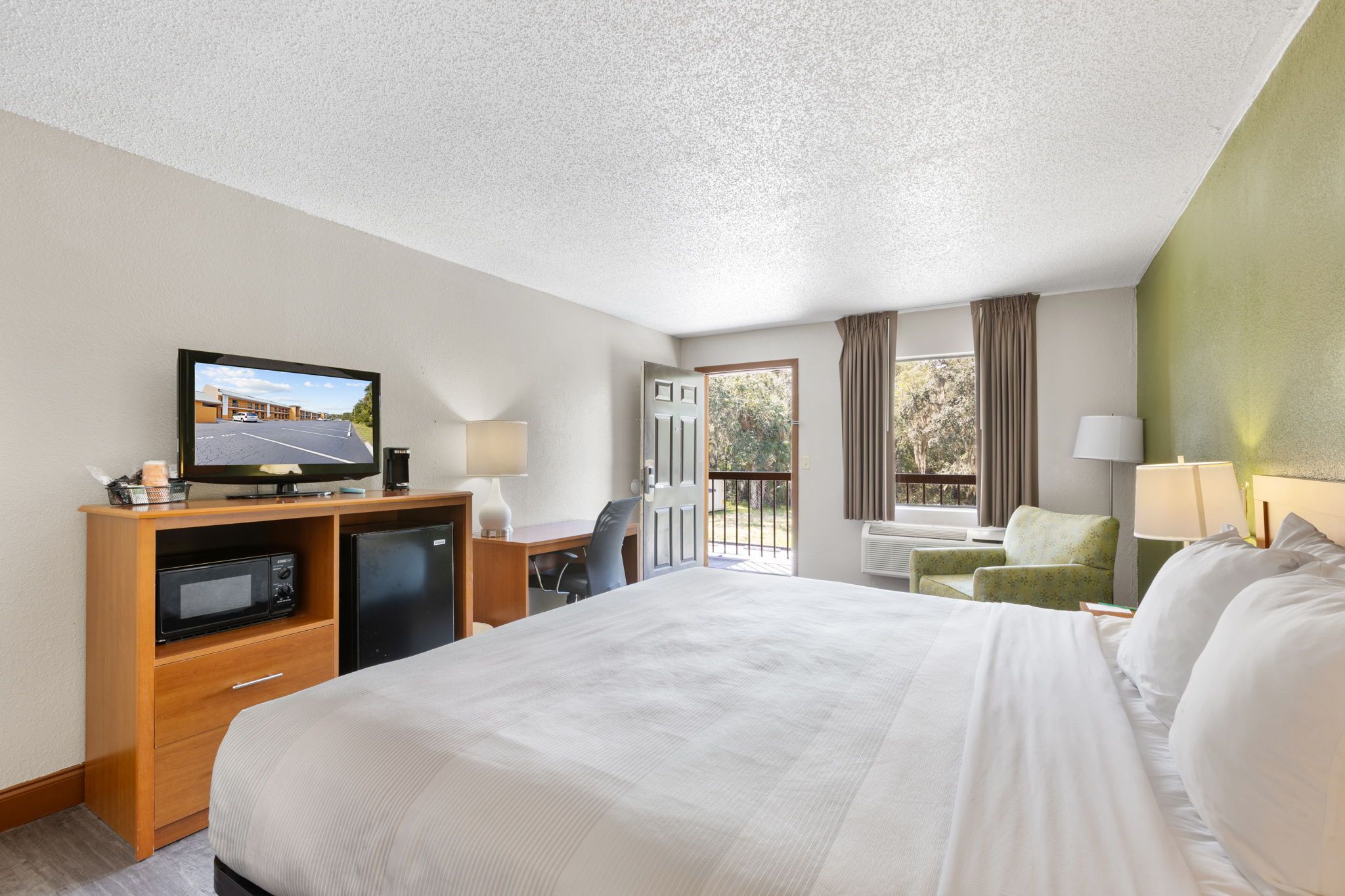 A hotel room with a bed, a desk with a computer, a television, and a window with curtains.
