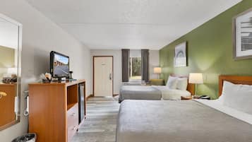 A hotel room with two beds, a desk with a television, a trash bin, and a door.