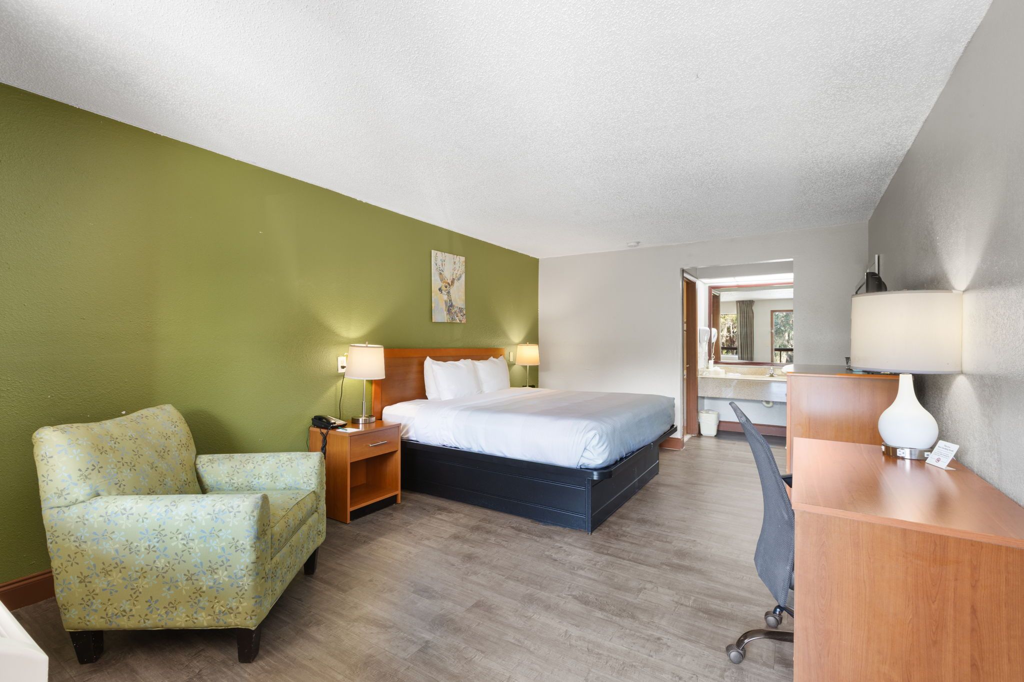Ein Hotelzimmer mit Bett, Schreibtisch, Stuhl, Nachttisch und Lampe.