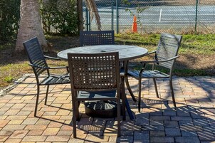 Una mesa metálica redonda con cuatro sillas, rodeada por un patio de ladrillo.