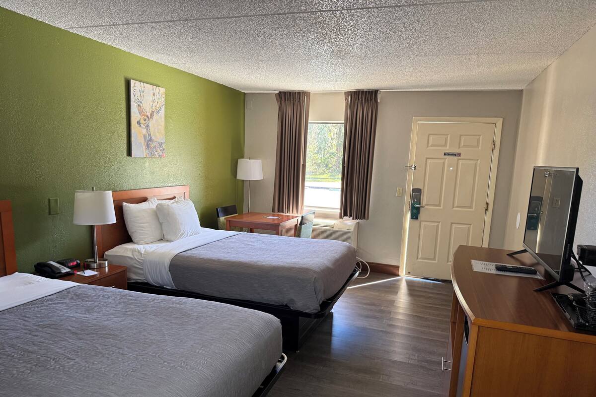 A hotel room with two beds, a desk, a TV, and a window with curtains.
