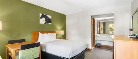 Habitación de hotel con cama, escritorio, silla, espejo y un cuadro en la pared.