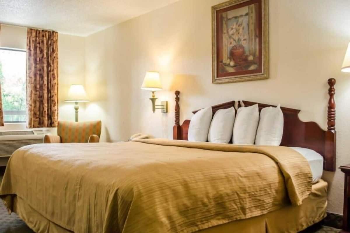 A hotel room with a large bed, two bedside lamps, a painting on the wall, and a window with curtains.