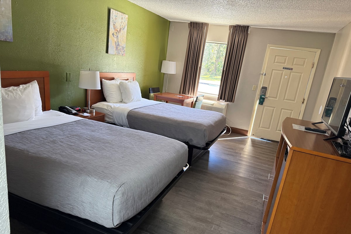 A hotel room with two beds, a desk with a computer, a lamp, and a painting on the wall.