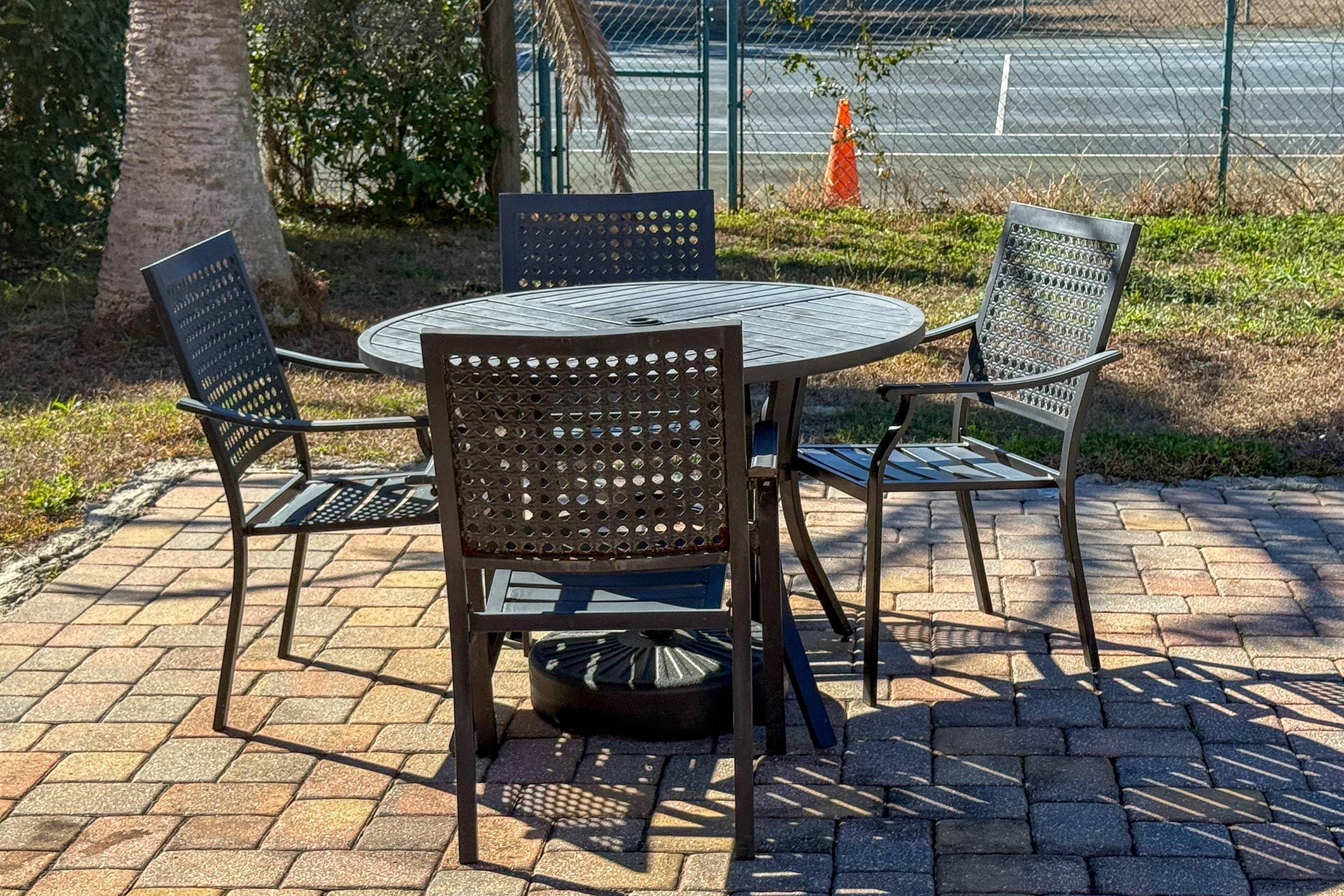 A round metal table with four chairs, surrounded by a brick patio.