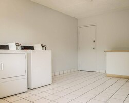 Un lavadero con dos lavadoras blancas, una puerta blanca y piso de baldosas.