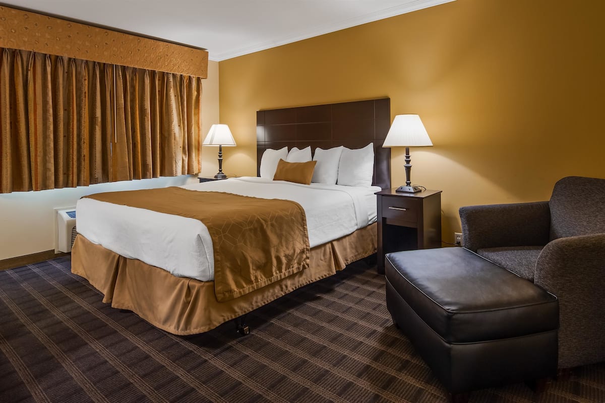 A hotel room with a large bed, two bedside lamps, a brown armchair, and a small table.