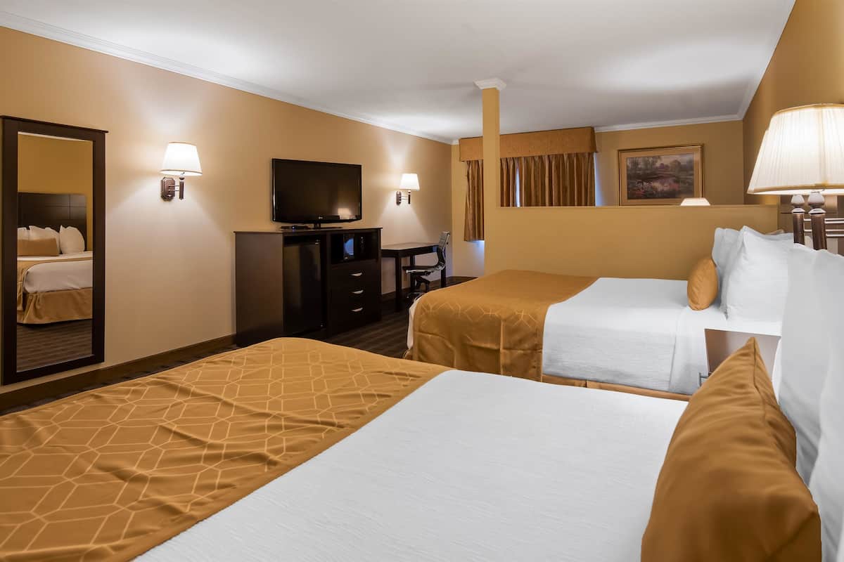 A hotel room with two beds, a desk, a television, and a mirror.