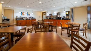 A clean, well-lit restaurant with wooden tables and chairs, a kitchen area, and a counter with a coffee machine. - Best Western Inn & Suites (Ontario)