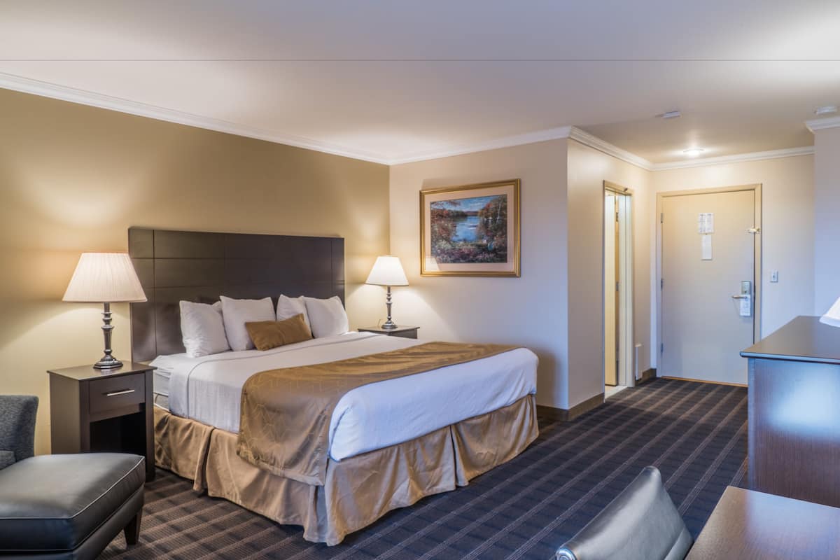 A hotel room with a large bed, two bedside tables with lamps, a desk, a chair, and a painting on the wall.