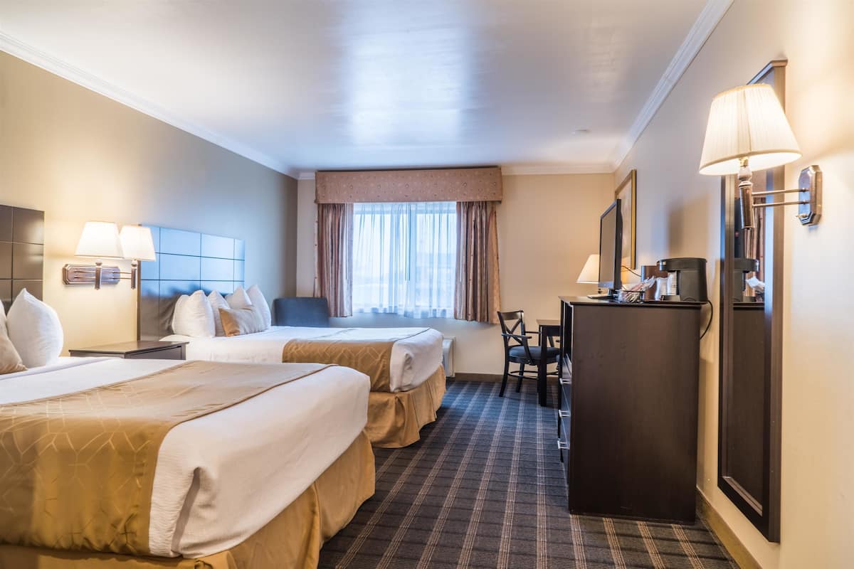 A hotel room with two beds, a desk, a chair, a lamp, and a window with curtains.