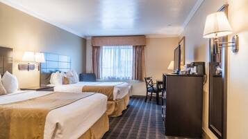 A hotel room with two beds, a desk, a chair, a lamp, and a window with curtains.