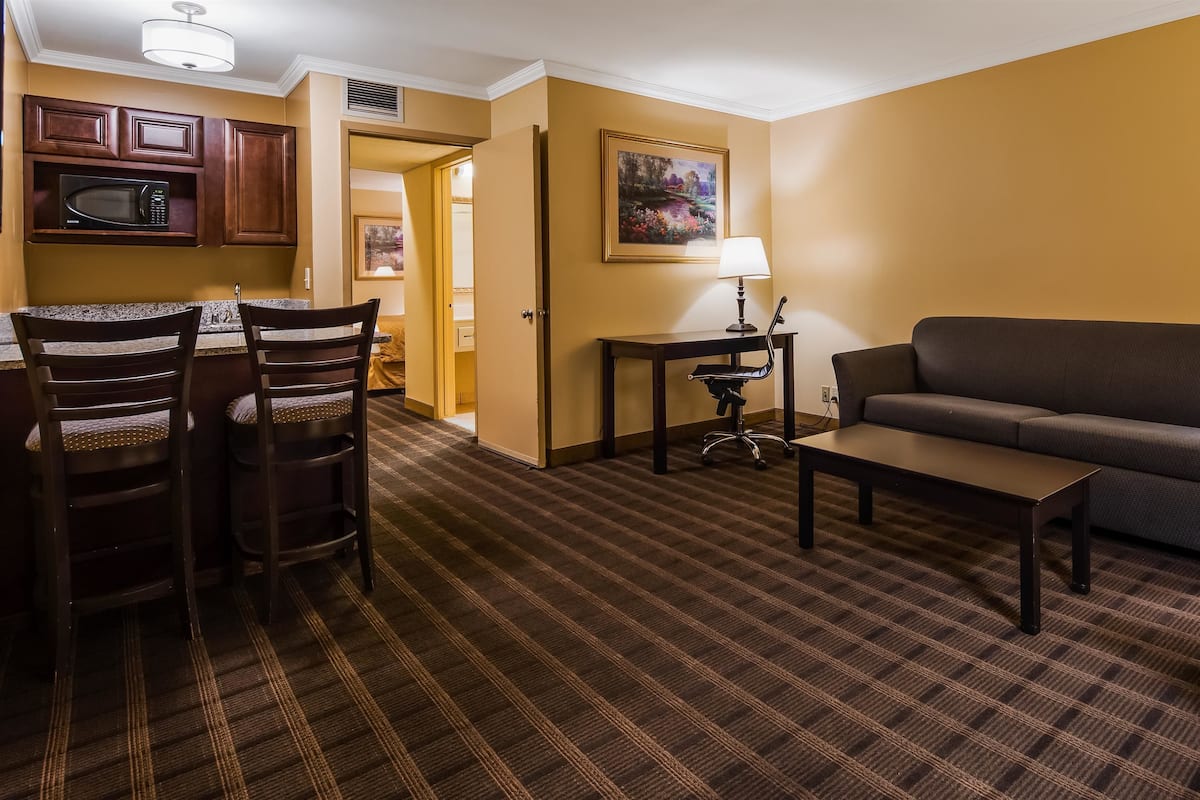 A hotel room with a dining area, a sofa, a lamp, and a painting on the wall.