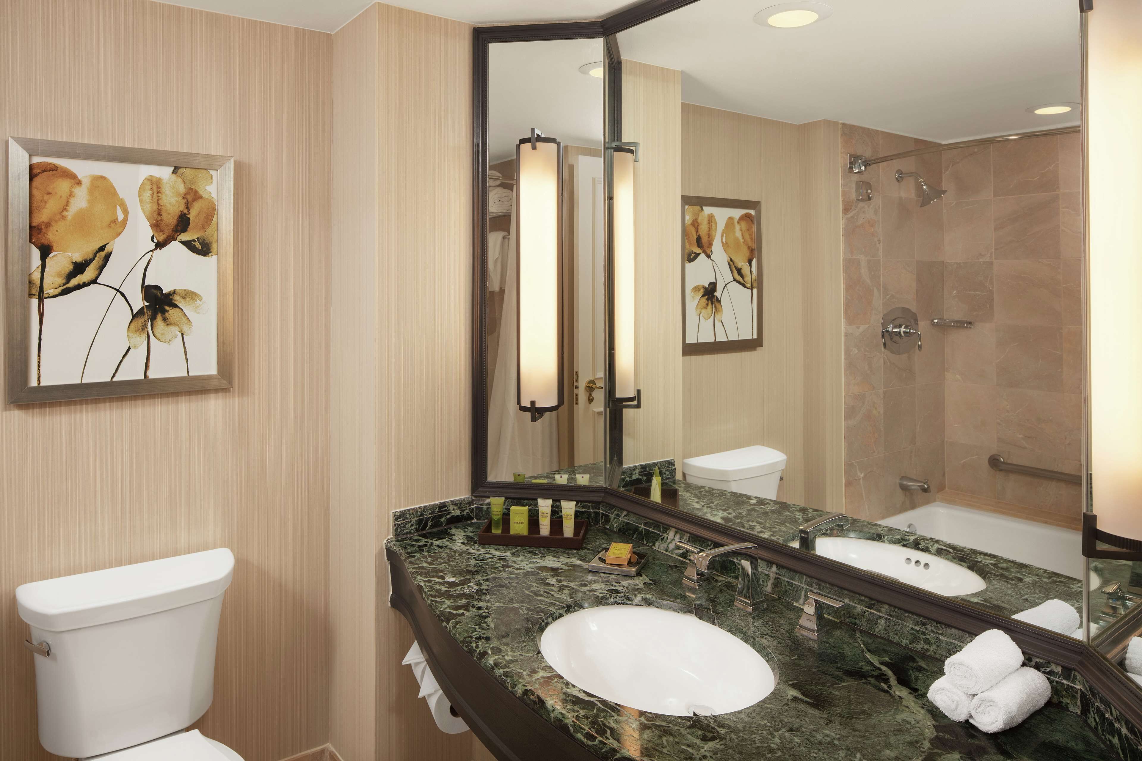 A bathroom with a marble sink, a toilet, a shower, and artwork on the walls.