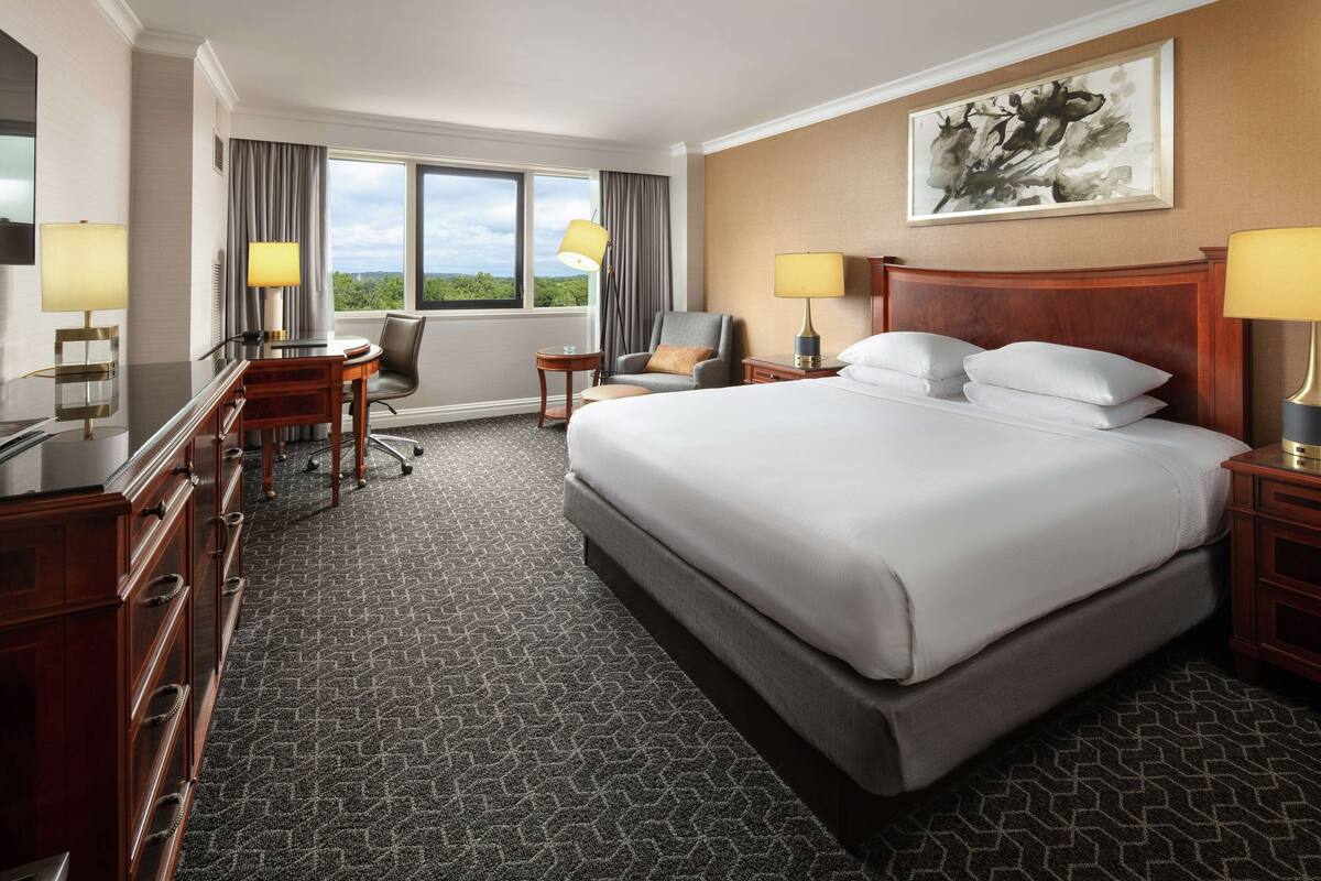 A hotel room with a large bed, a desk, a chair, a TV, and a window with curtains.
