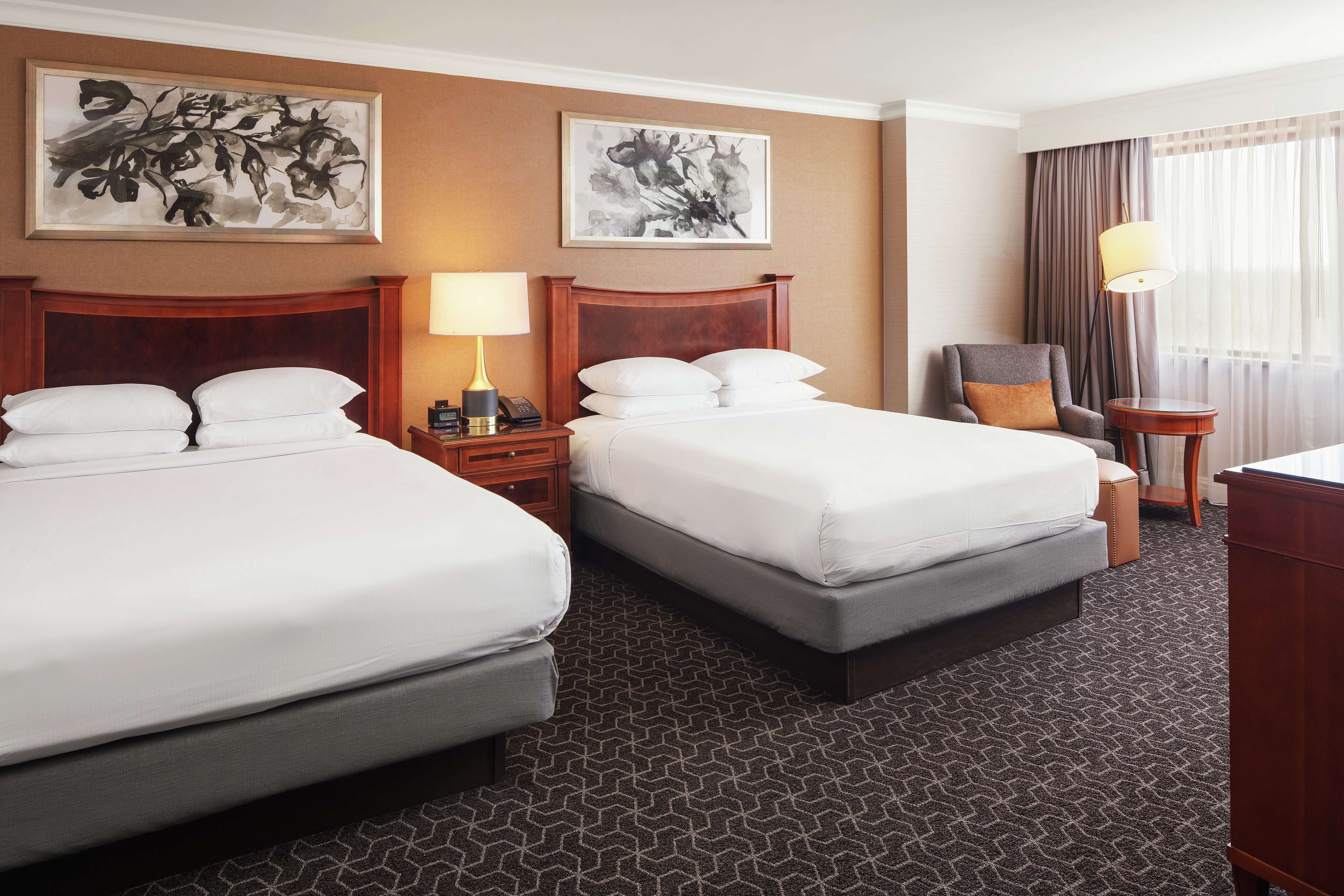 A hotel room with two beds, a desk, a chair, and artwork on the walls.