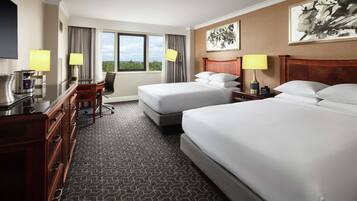 A hotel room with two beds, a desk, a chair, a coffee maker, and a large window with a view.