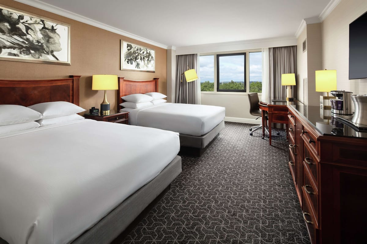 A hotel room with two beds, a desk, a chair, a TV, and a window with a view.