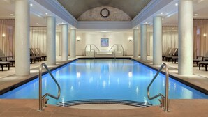 A large indoor swimming pool with clear blue water, surrounded by columns and seating areas.