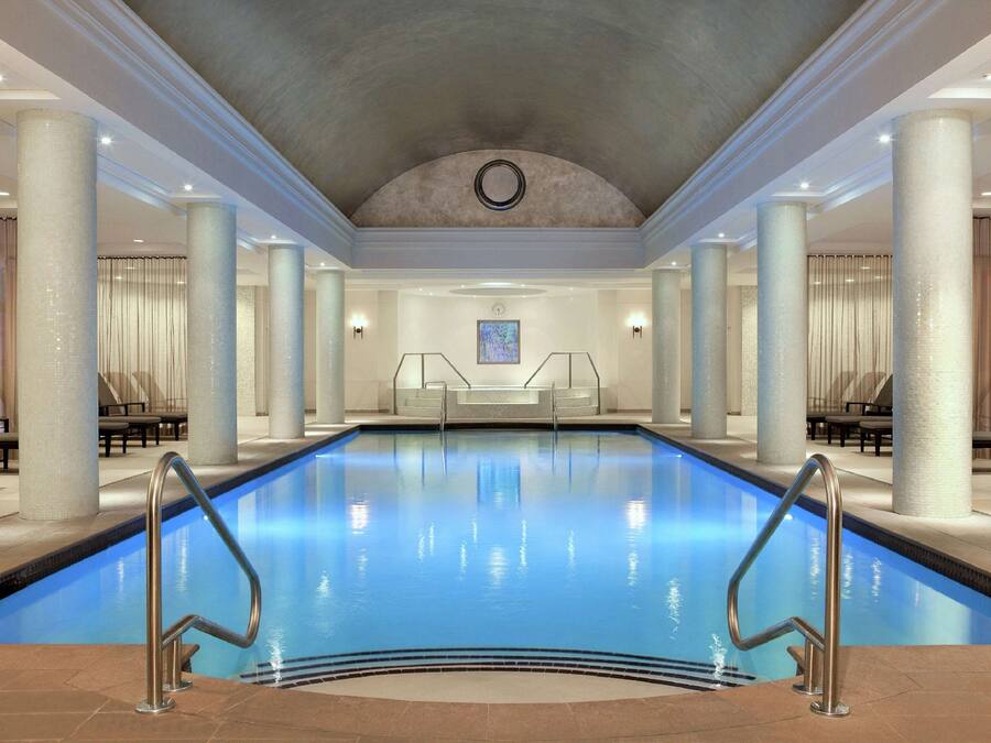 A large indoor swimming pool with clear blue water, surrounded by columns and seating areas.