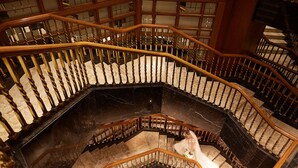 A grand, spiral staircase with marble steps and wooden railings, leading to an upper floor.