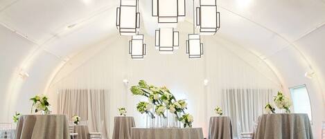 A tented event space with tables covered in tablecloths, chairs, and floral centerpieces.