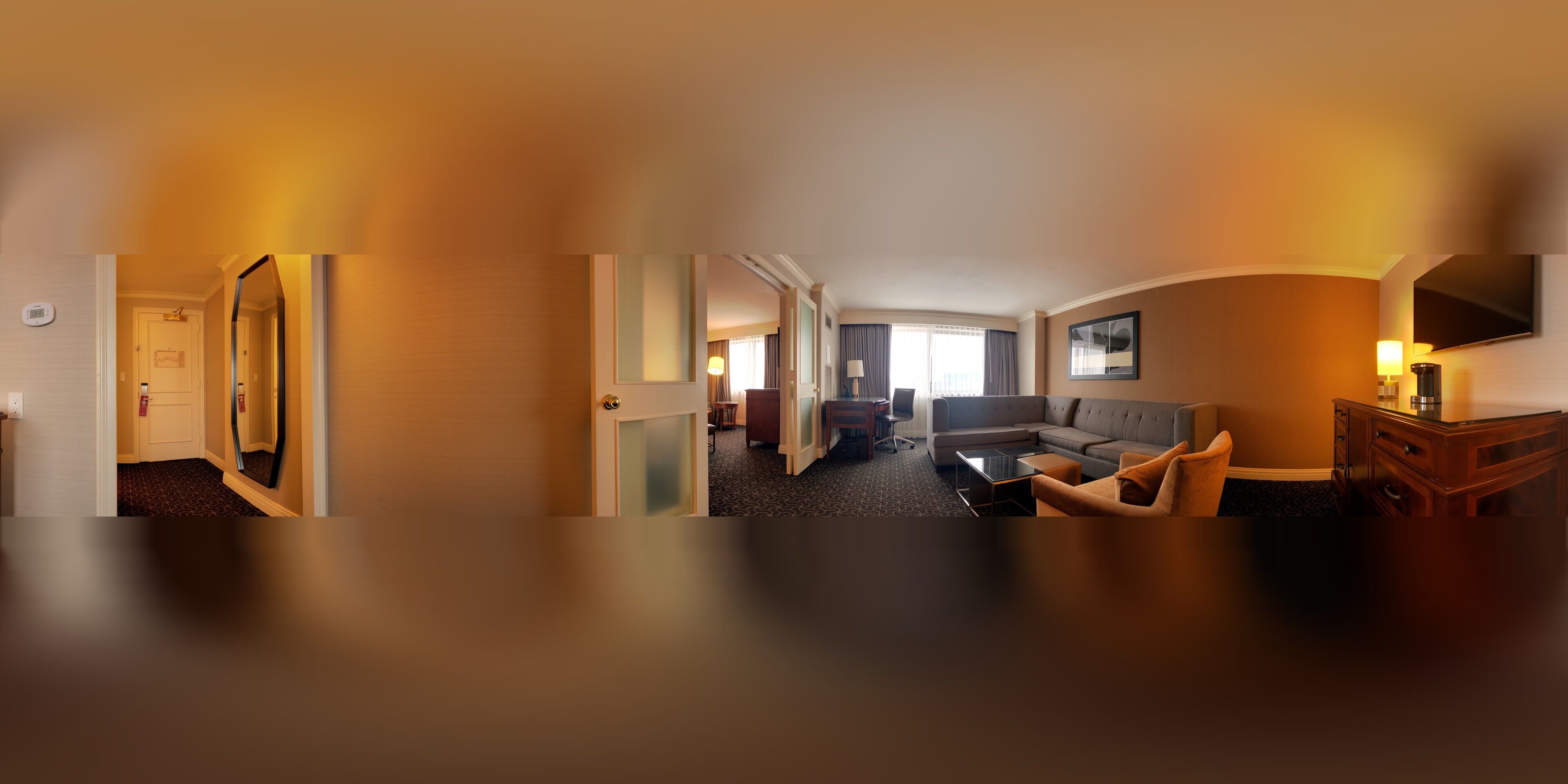 A hotel room with a living area, a sofa, a coffee table, a TV, and a desk with a lamp.
