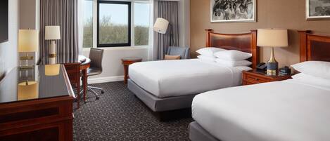 A hotel room with two beds, a desk, a chair, a TV, and a window with curtains.