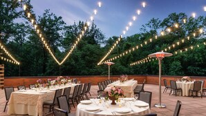 An outdoor dining area with tables set for a meal, surrounded by trees and string lights.