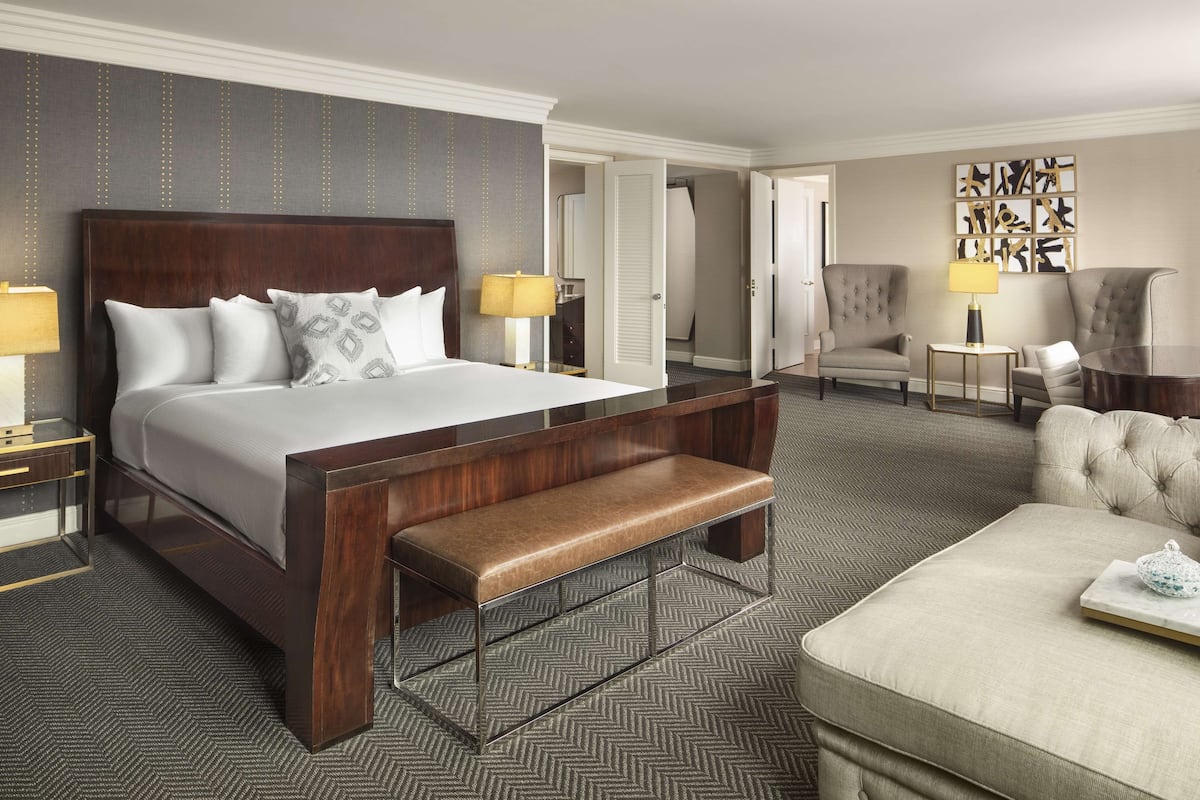 A hotel room with a large bed, a bench, a sofa, a desk, and a chair.