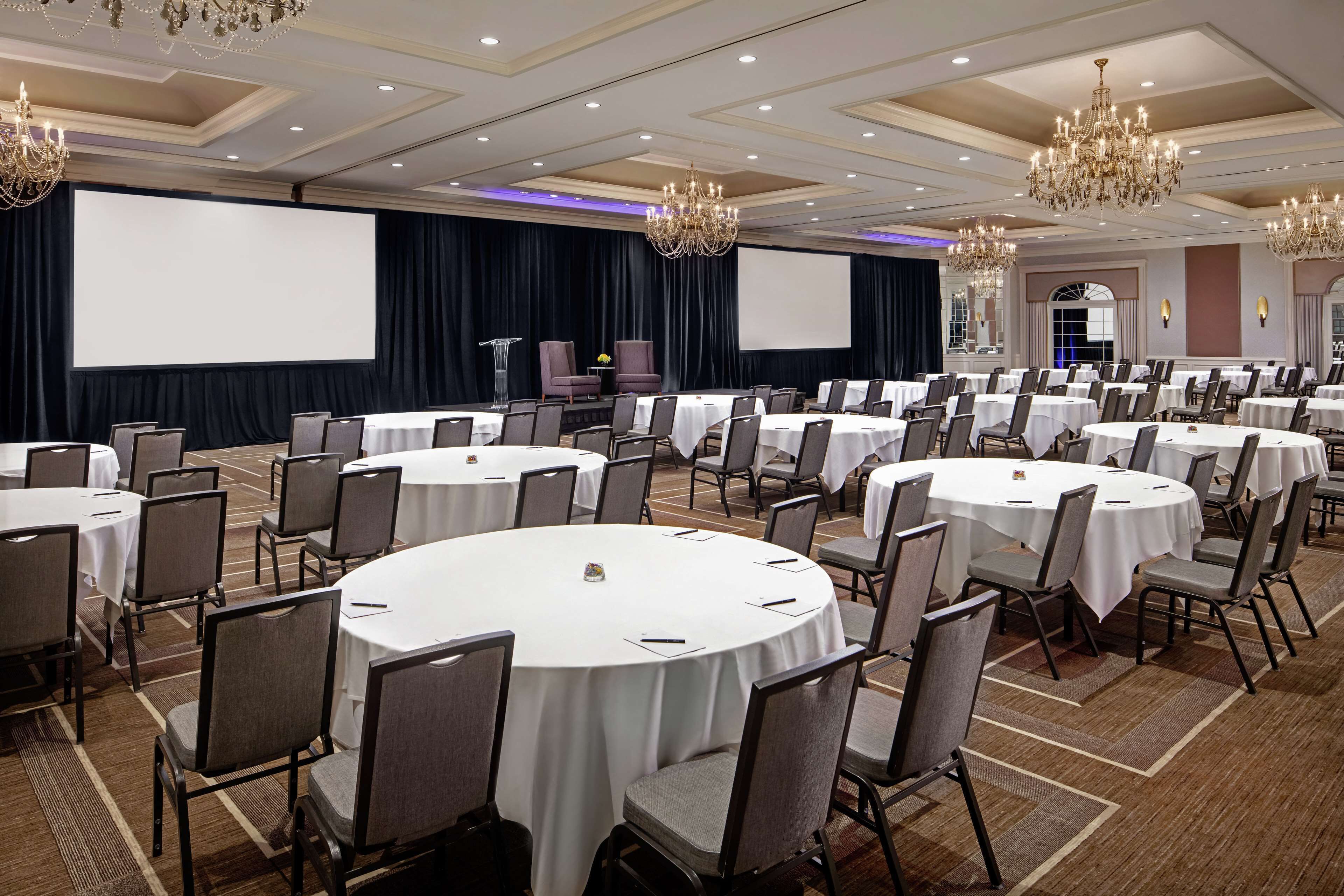 A conference room with round tables, chairs, and a large screen.