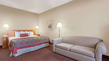 Habitación de hotel con cama, sofá, dos lámparas de noche, un cuadro en la pared y alfombra estampada.