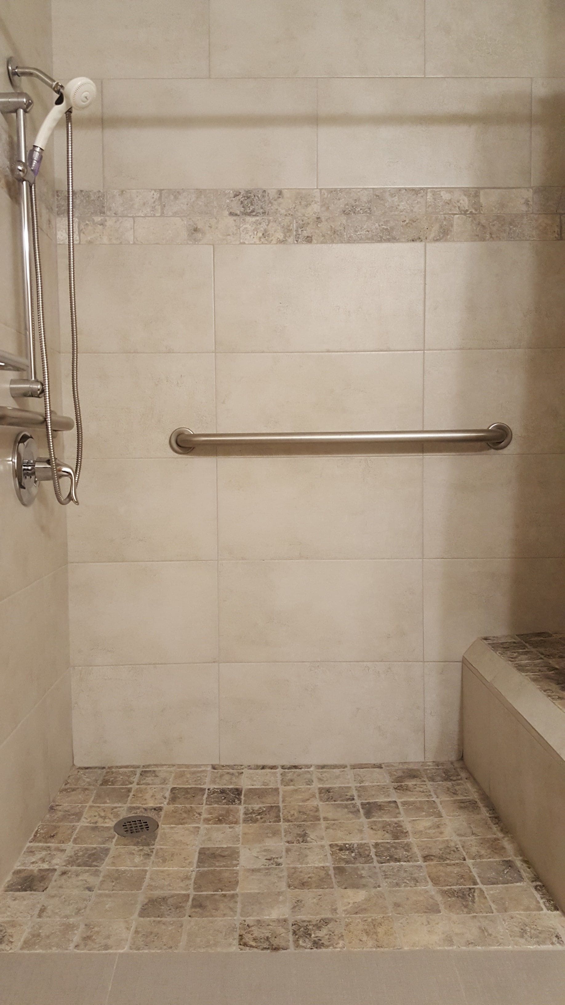 A shower area with a grab bar, tiled walls, and a tiled floor.
