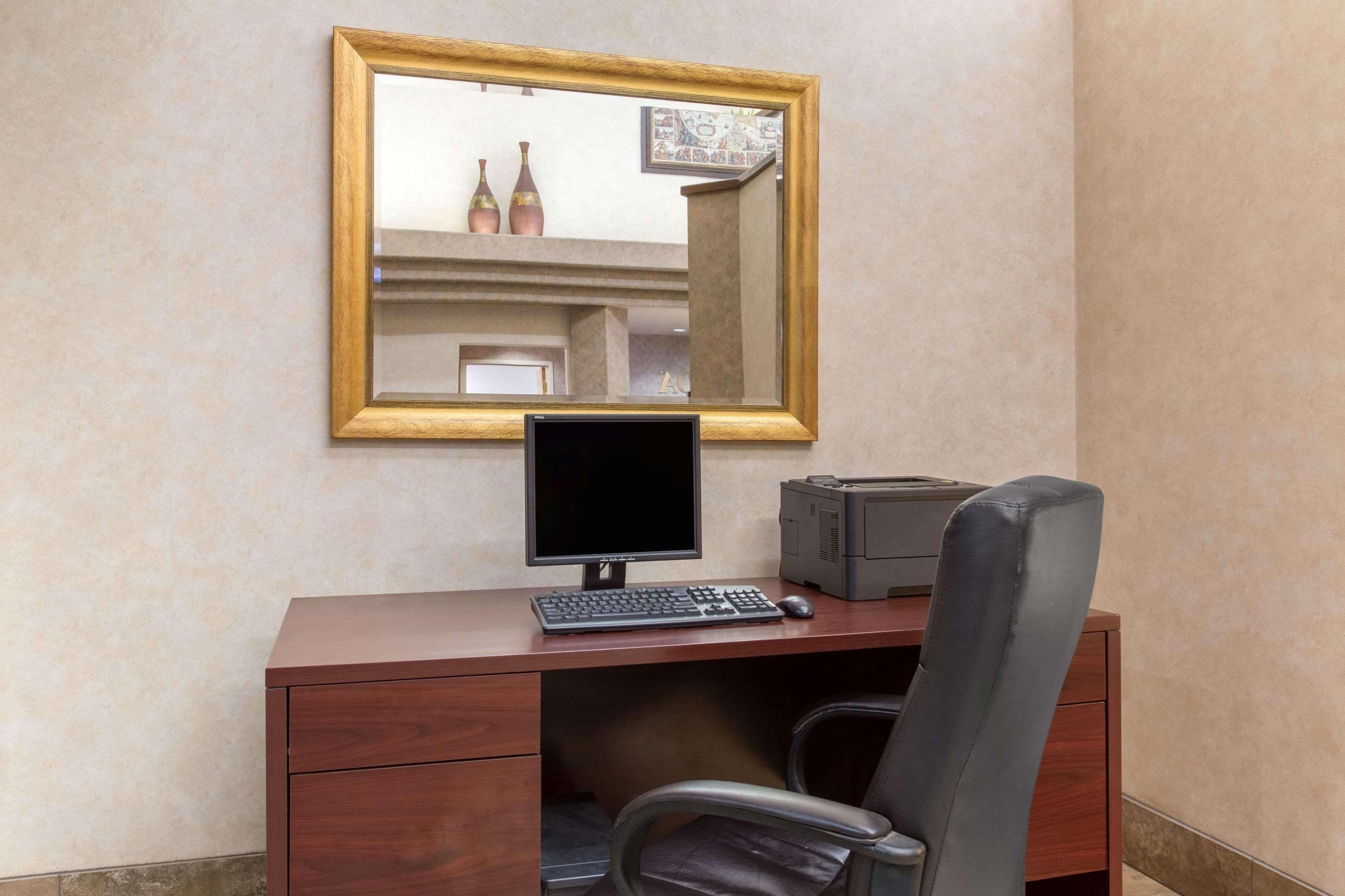 A wooden desk with a computer monitor, keyboard, and printer. A chair is positioned in front of the desk.