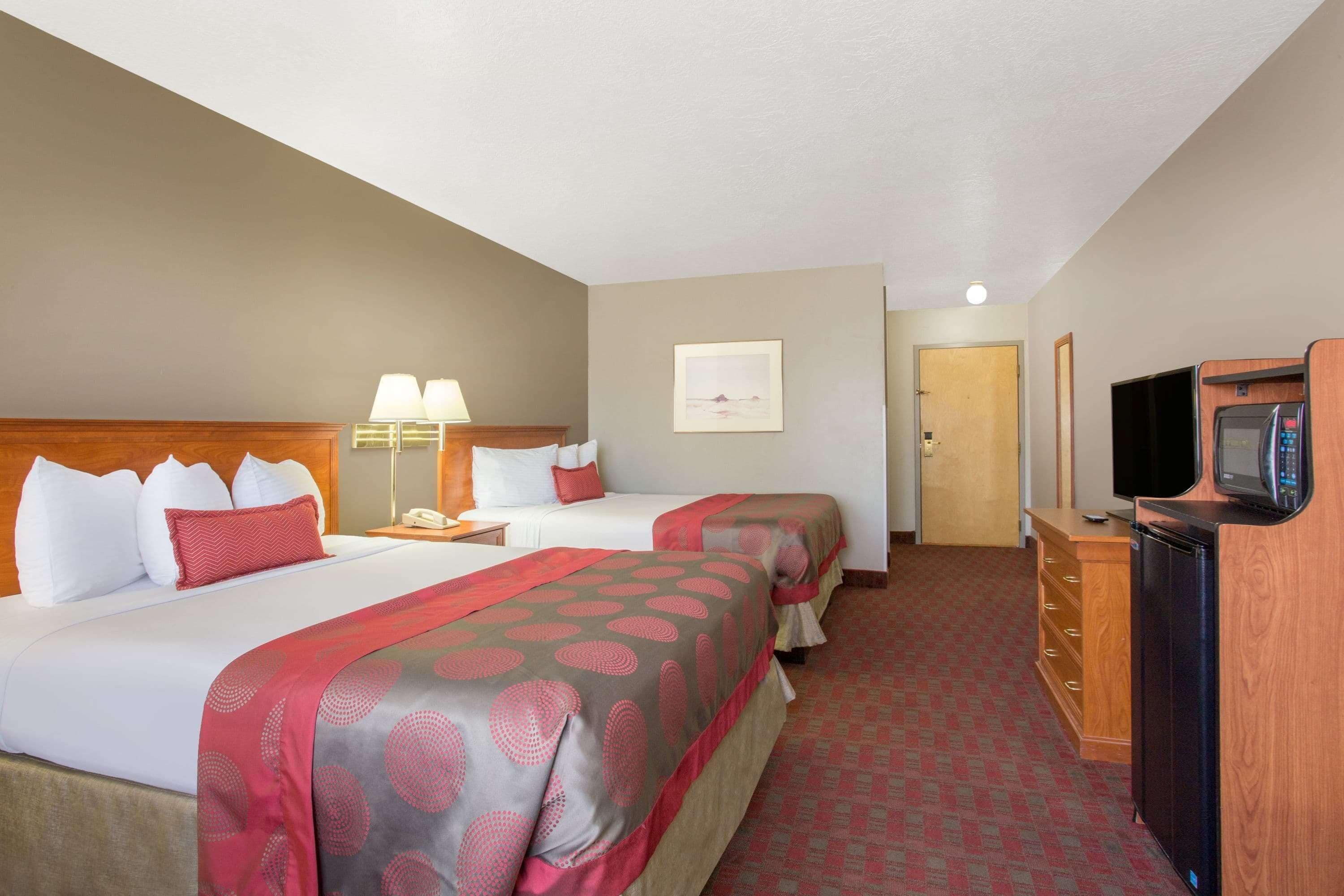 A hotel room with two beds, a desk with a lamp, a television, and a microwave.