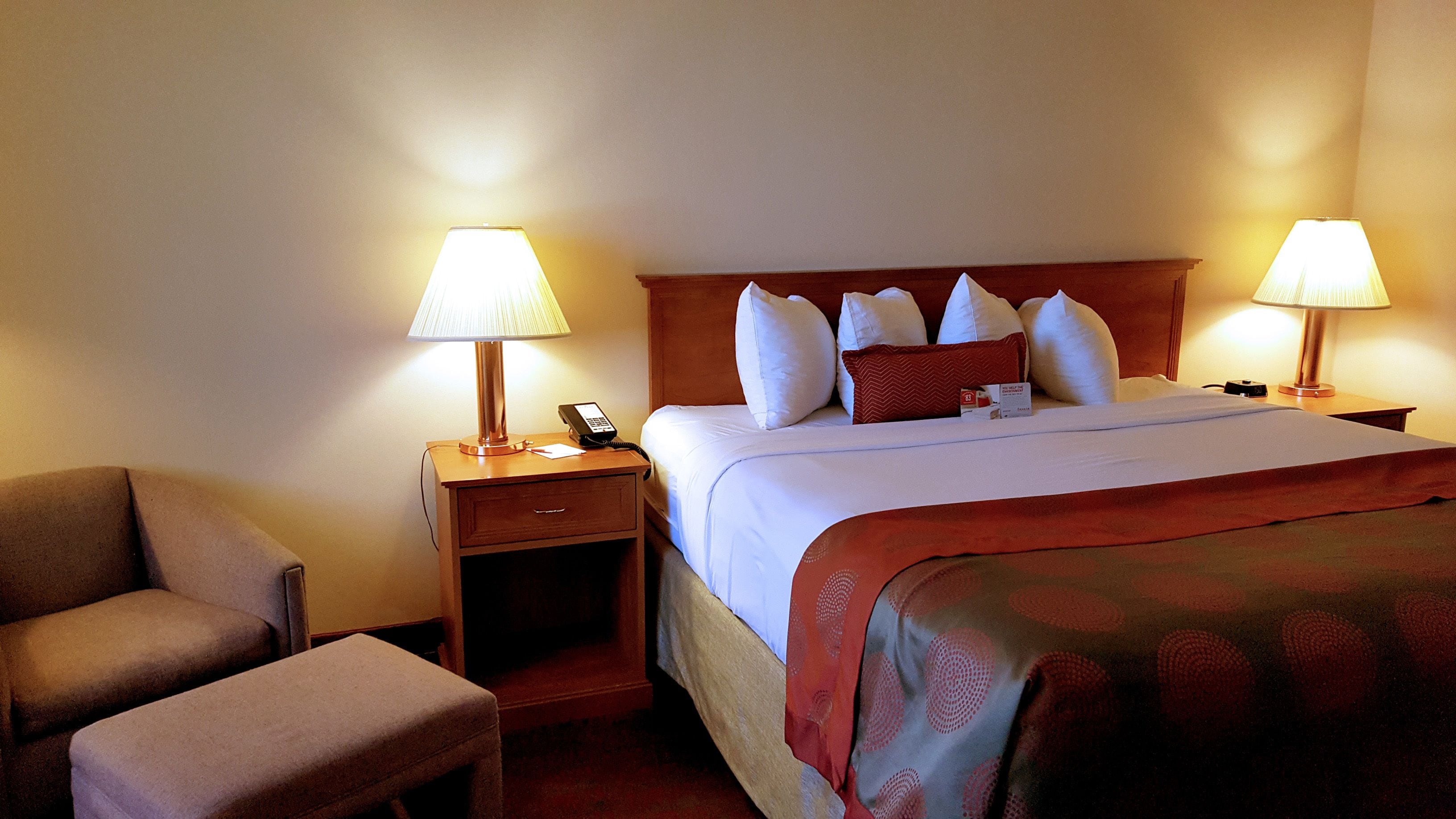 A hotel room with a bed, two bedside tables, a chair, and two lamps.