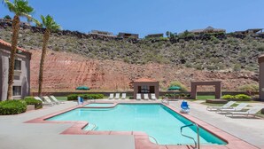 A swimming pool with lounge chairs and a small gazebo, surrounded by palm trees and a hilly landscape.