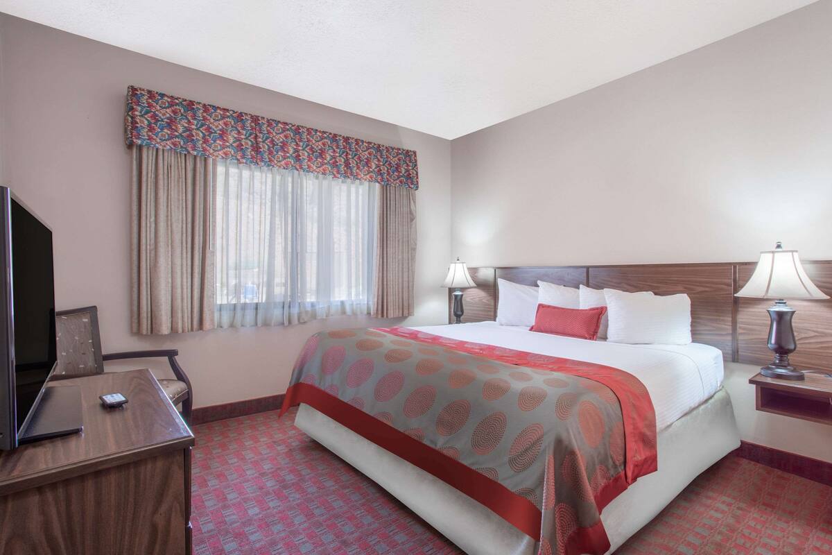 A hotel room with a large bed, two bedside lamps, a desk with a TV, and a window with curtains.
