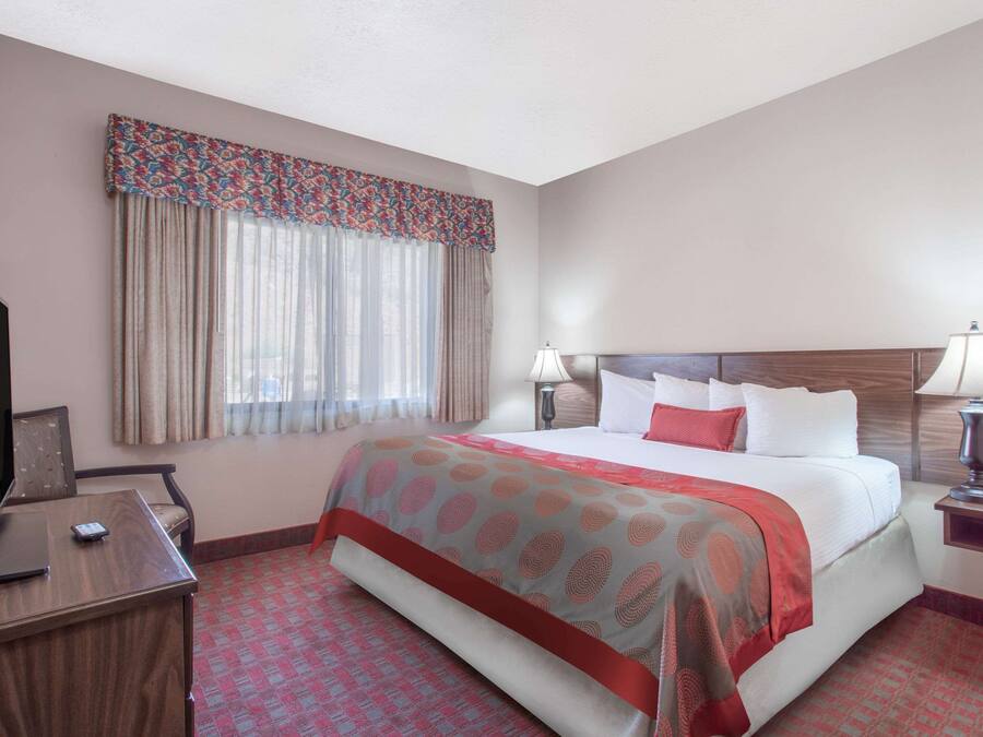 Une chambre d’hôtel avec un grand lit, deux lampes de chevet, un bureau avec une télévision et une fenêtre avec des rideaux.
