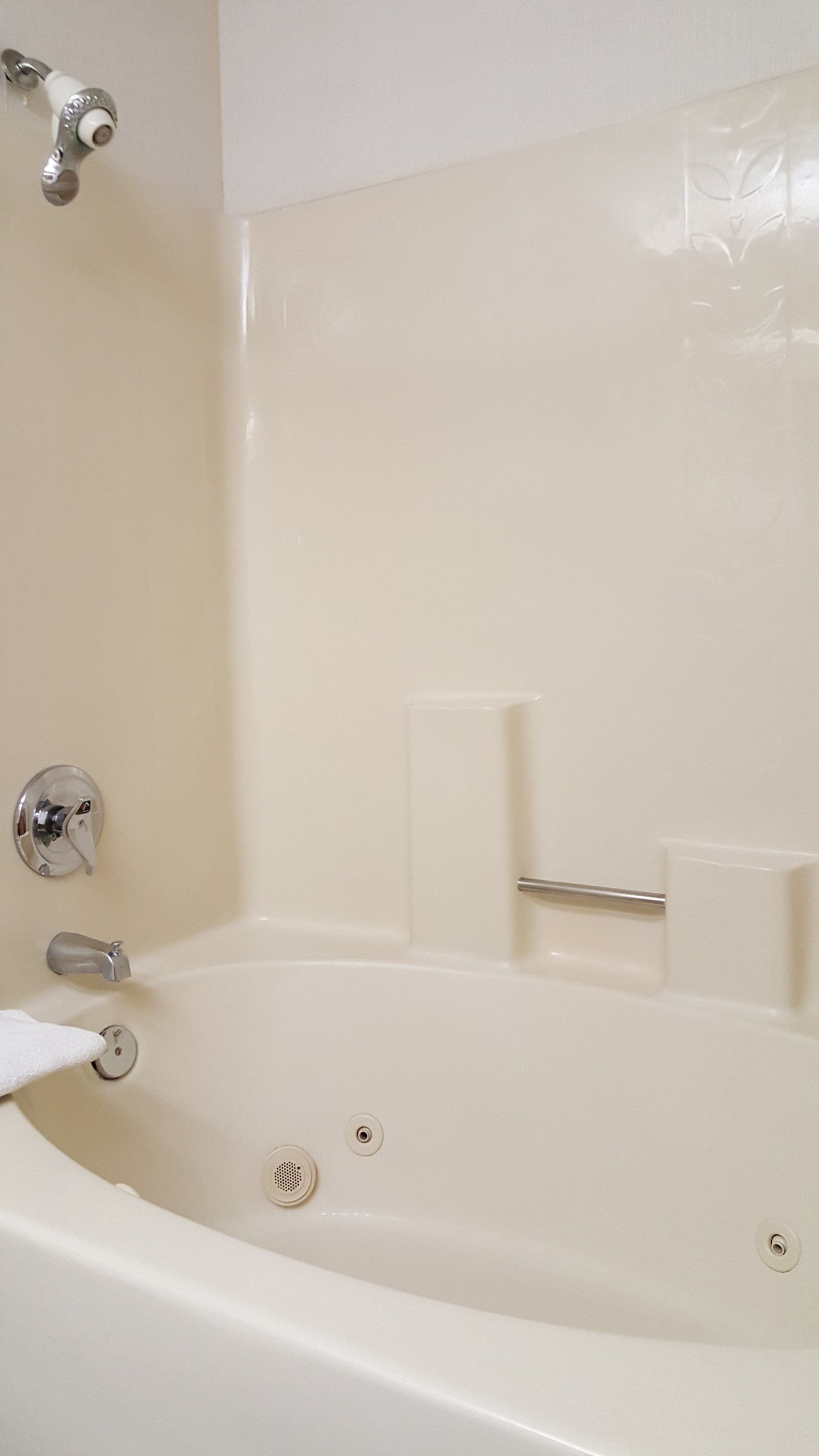 A white bathtub with chrome fixtures, a handheld showerhead, and a small shelf.