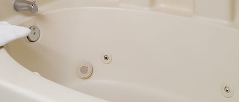 A white bathtub with chrome fixtures, a handheld showerhead, and a small shelf.