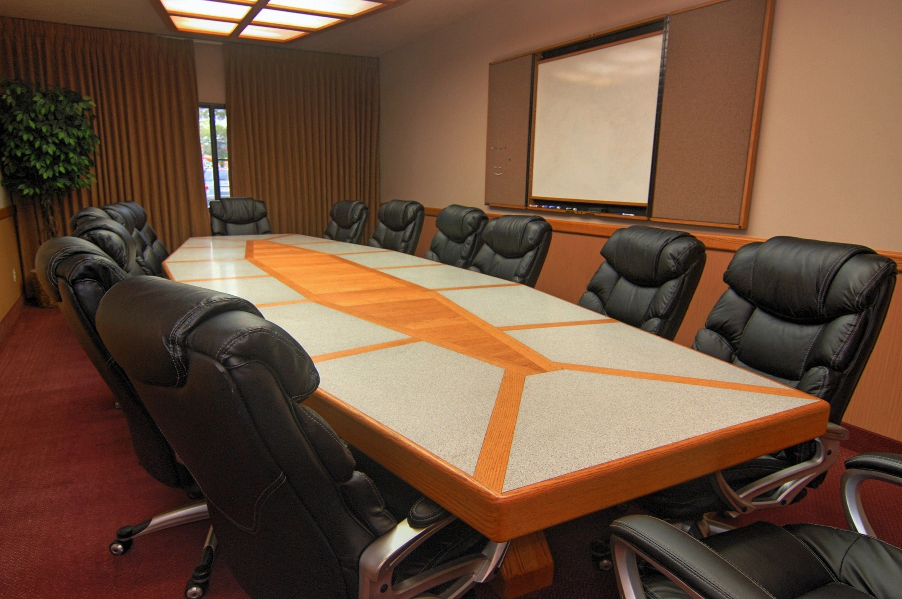 A conference room with a long table, black leather chairs, a projector screen, and a potted plant.