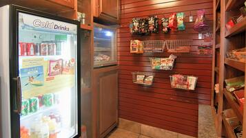 Máquina expendedora de bebidas frías con diversas opciones y una pared exhibidora con bolsas de aperitivos.