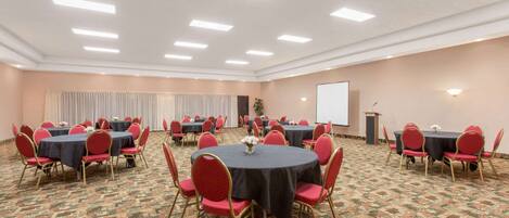 A conference room with round tables and red chairs, carpeted floor, and a projector screen.