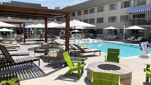 A rooftop pool area with lounge chairs, umbrellas, and a fire pit.